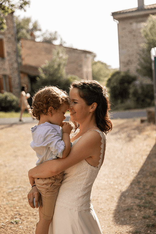 Une jeune mariée porte son enfant dans les bras