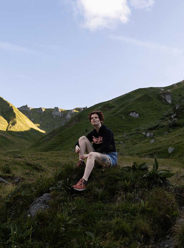 une jeune femme assise dans l'herbe avec les montagnes en fond