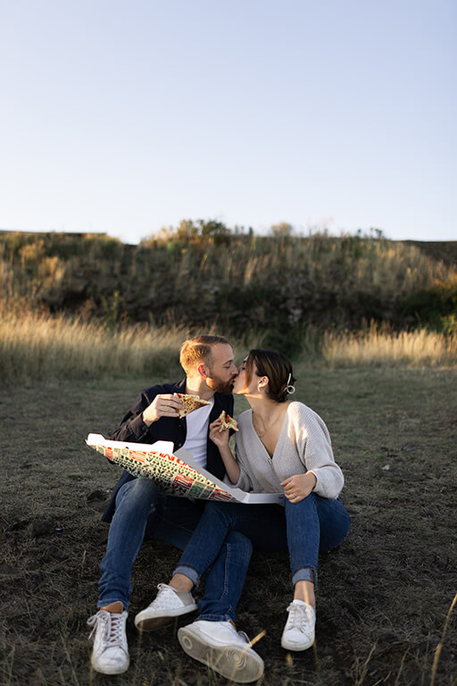 un couple mange une pizza et s'embrasse, assis dans l'herbe