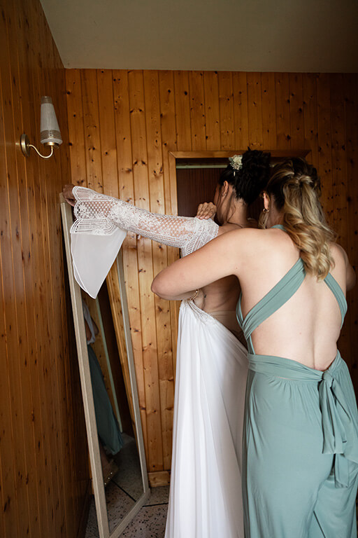 une femme aide une mariée à enfiler sa robe