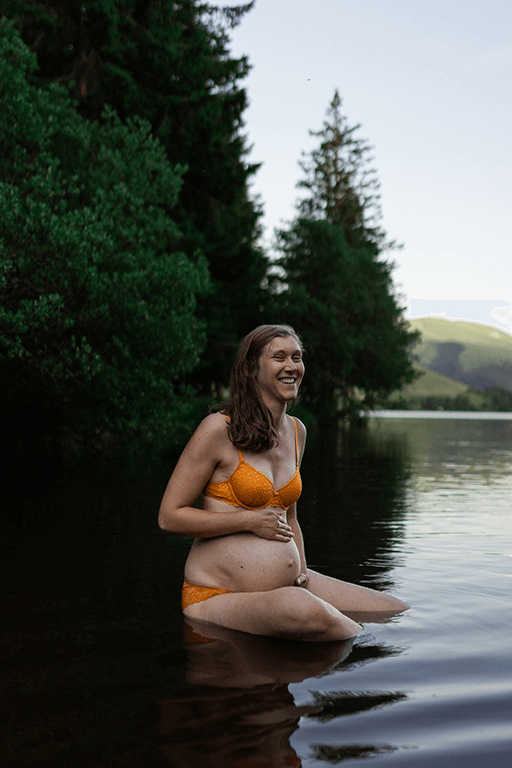 Une femme rigole lors d'une séance photo de grossesse dans un lac d'Auvergne