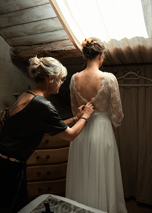 une mariée se fait aider à attacher sa robe de mariée