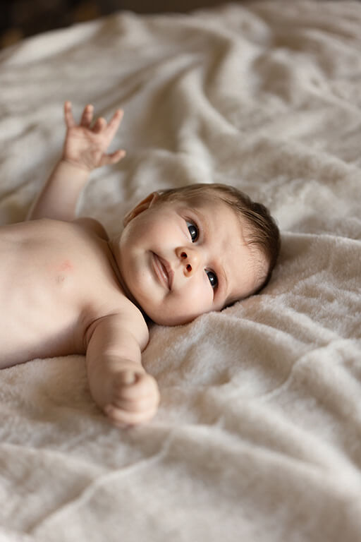 un bébé écarte les bras, étendu sur un lit