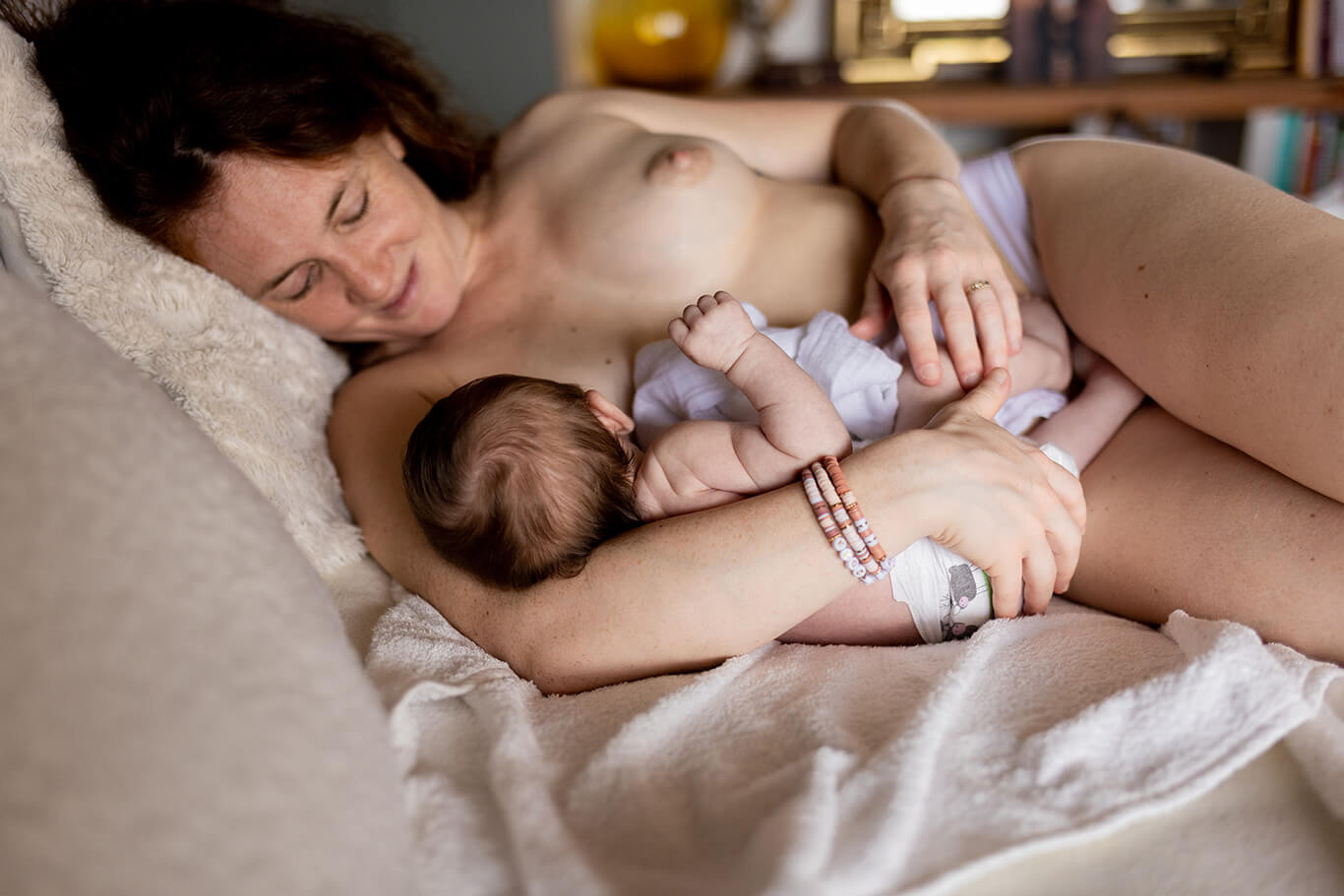 Une jeune femme allaite son bébé allongée sur son lit