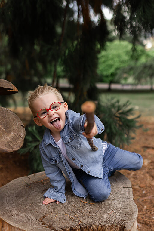 un enfant joue avec un bout de bois sur un tronc d'arbre coupé
